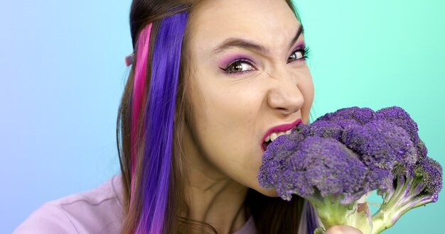 Foto giovane donna con i capelli viola che morde broccoli viola primo piano del viso