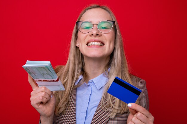 お金の札束と赤い背景の上の銀行カードを持つ若い女性