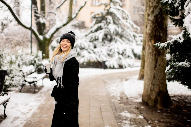 Young woman with Warm Clothes in Cold Winter Snow drinking coffee to go