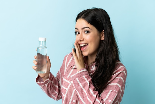 Giovane donna con un'acqua isolata su sfondo blu sussurrando qualcosa