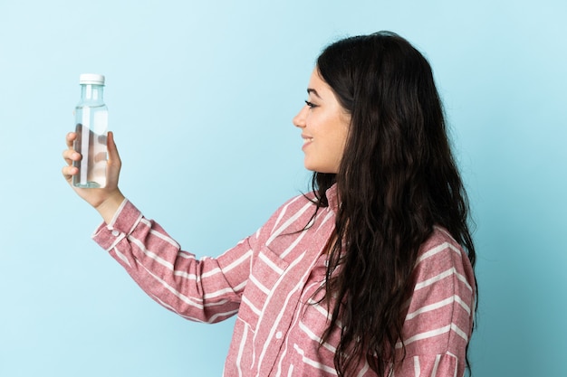 Giovane donna con un'acqua isolata sulla parete blu con l'espressione felice