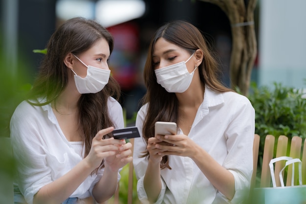 Giovane donna con indossare la maschera protettiva parlando e ridendo tenendo la carta di credito