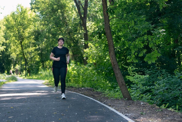 体重過剰の若い女性が公園を走ります。曲線美の女の子は、余分な体重を減らすためにスポーツに参加します。