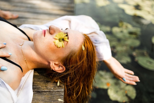 Photo young woman with wet red hair lying on wooden bridge in summer