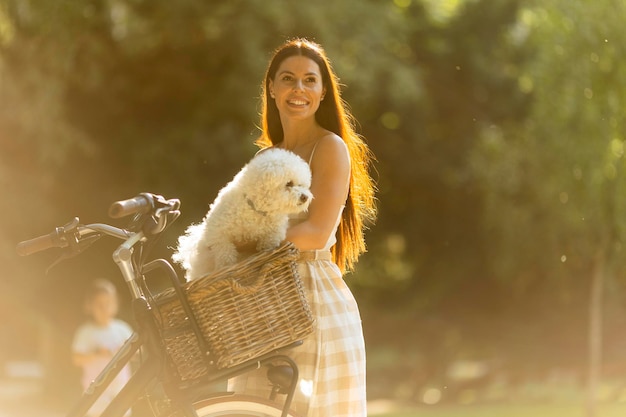 電動自転車のバスケットに白いビションフリーゼ犬と若い女性