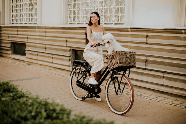 Молодая женщина с белой собакой бишон фризе в корзине электрического велосипеда