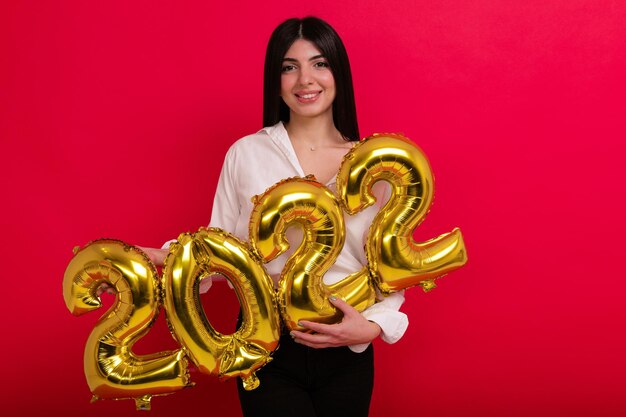 A young woman with a white shirt holds the numbers of the upcoming new year 2022