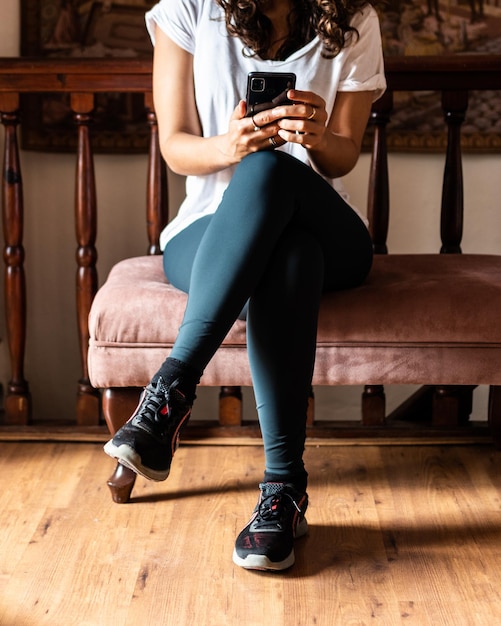 Young woman with white t-shirt sitting on a vintage chair with a smartphone