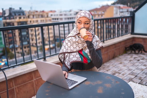 young woman with a white veil at the computer on the terrace of a coffee shop, doing work