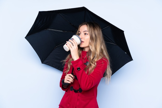 傘と持ち帰るコーヒーを保持している冬のコートを持つ若い女性