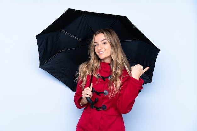 Young woman with winter coat and  holding an umbrella pointing to the side to present a product