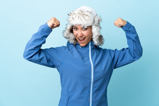 Young  woman with winter hat isolated on blue space celebrating a victory