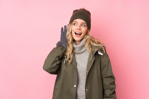 Young woman with winter hat isolated on pink wall listening something