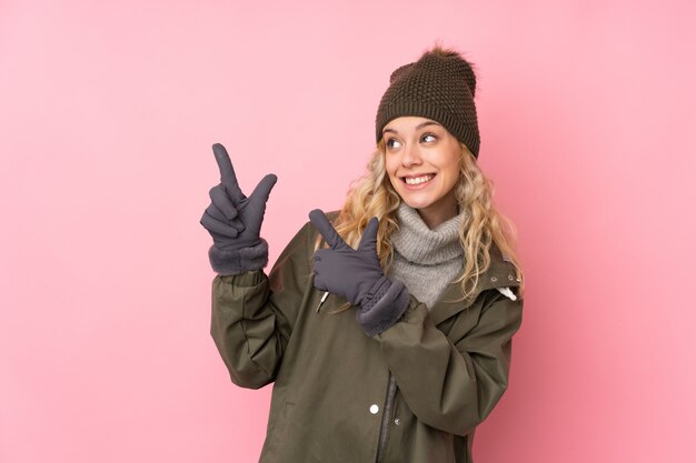 Young woman with winter hat isolated on pink wall pointing with the index finger a great idea