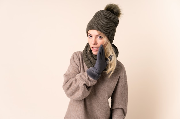 Young woman with winter hat over isolated whispering something