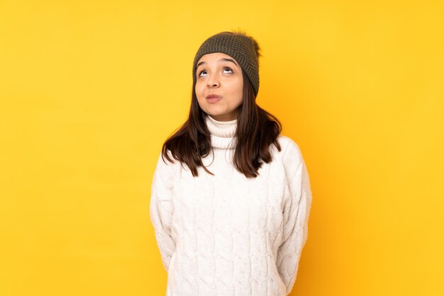 黄色の壁と見上げる冬の帽子を持つ若い女性