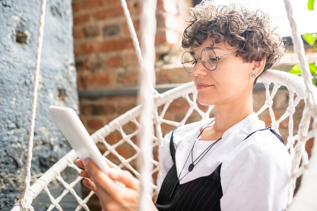 Young woman with wireless gadget looking at display while watching online video or movie at leisure at home