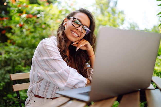 Young woman with wireless headphones calling on laptop talk by webcam video conference on cafe