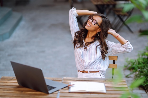 Young woman with wireless headphones calling on laptop talk by webcam video conference on cafe