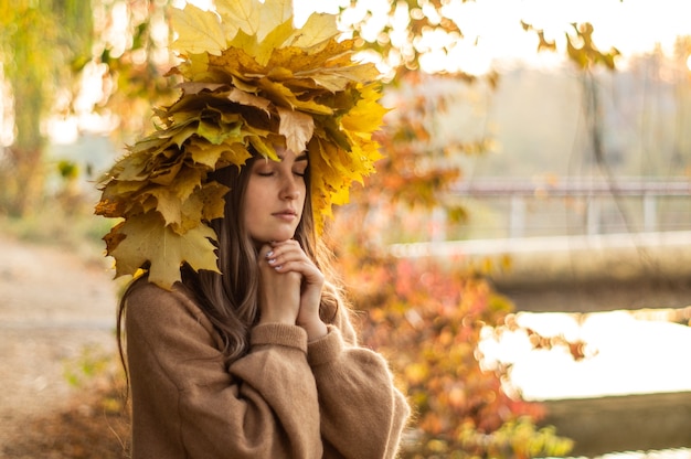 黄色い紅葉の花輪を持つ若い女性。屋外の肖像画。秋。