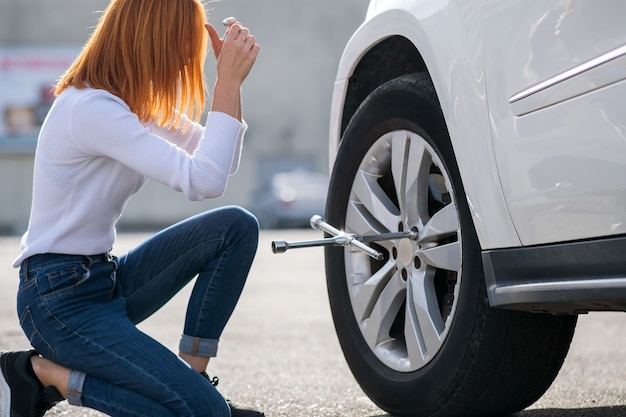 壊れた車のホイールを変更するレンチを持つ若い女性。