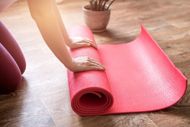 Young woman with yoga mat indoors, fitness healthy and sport concept. Woman rolling her Yoga mat after a workout.