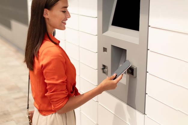 Young woman withdrawing money at atm using phone in city