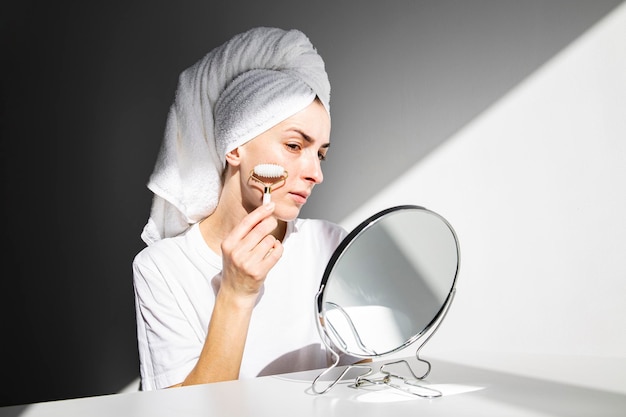 Young woman without makeup doing face massage with roller massager