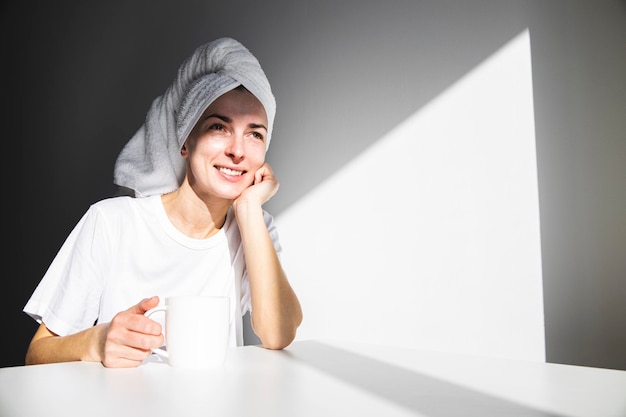 Young woman without makeup with a towel on her head drinking morning coffee or tea