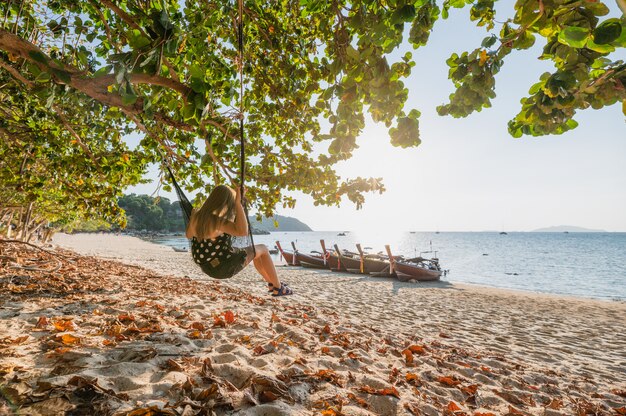 Young woman on wooden swing on the beach in tropical sea