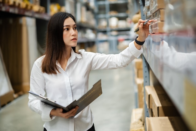 Foto lavoratore della giovane donna che tiene appunti e controllo dell'inventario nel magazzino del magazzino