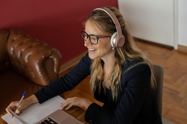 Foto giovane donna che lavora a casa con laptop e documenti sulla scrivania e cuffie concetto di ufficio a casa quaderno grigio per il lavoro persona foto di alta qualità