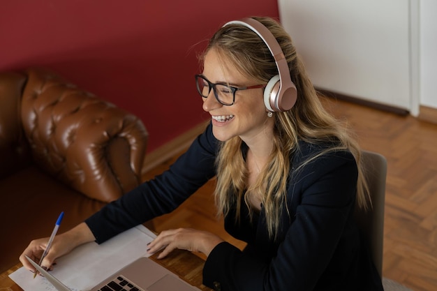 Foto giovane donna che lavora a casa con laptop e documenti sulla scrivania e cuffie concetto di ufficio a casa quaderno grigio per il lavoro persona foto di alta qualità