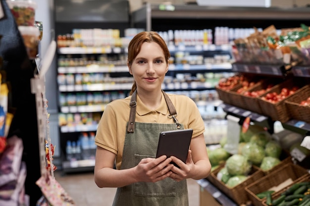 Фото Молодая женщина, работающая в супермаркете и улыбающаяся в камеру с планшетом