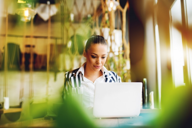 Young woman working on laptop at cafe bar.