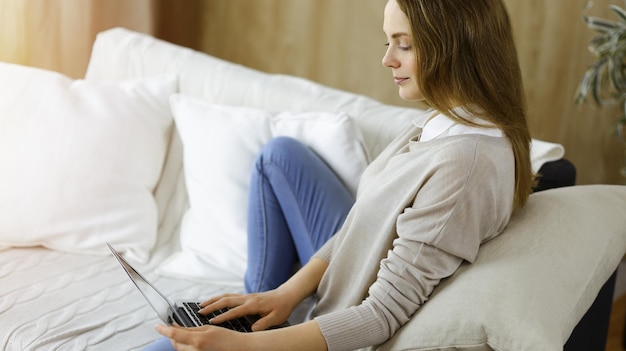 Young woman working on laptop computer sitting indoors during Covid-19 quarantine. Stay at home concept at Coronavirus pandemic.