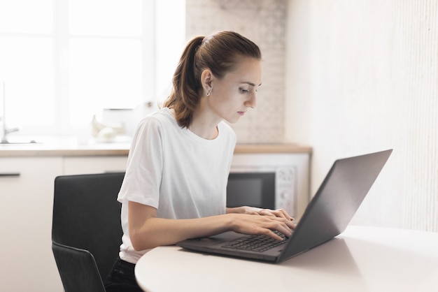Молодая женщина, работающая на ноутбуке на кухне. Женский фрилансер, работающий онлайн дома