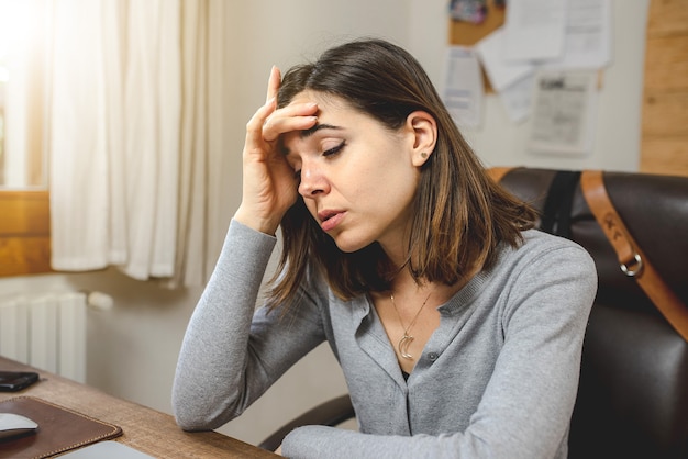 Giovane donna che lavora o studia alla scrivania stanco e stressato mette la mano sulla testa.