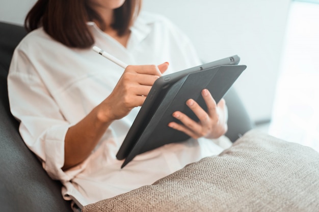 Young woman working on tablet computer while sitting at the living room.