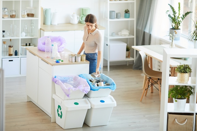 Young woman working with garbage while standing at her kitchen she separating the waste