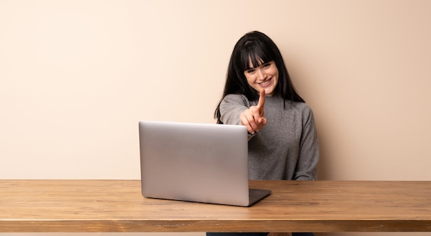 Young woman working with her laptop showing and lifting a finger