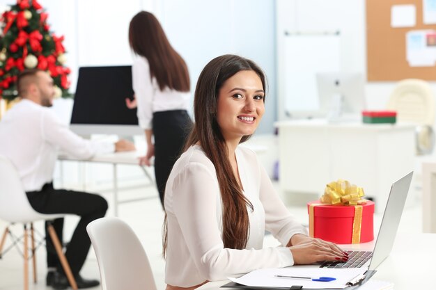 Young woman working with laptop in office decorated for Christmas