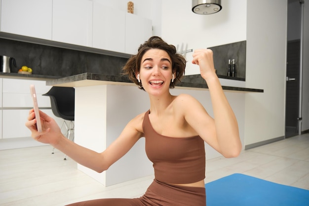 Молодая женщина тренируется дома, радуясь, используя спортивное приложение для смартфона, онлайн-видеозаписи с фитнеса
