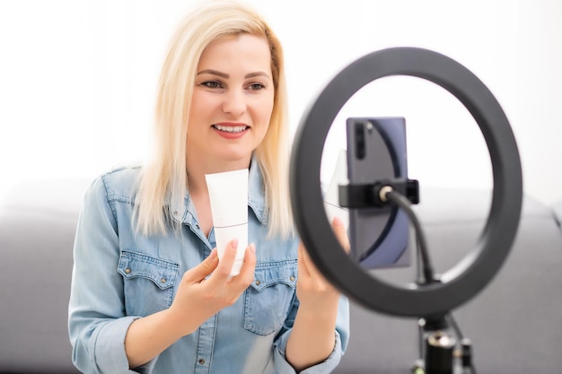 A young woman works, conducts live broadcasts from home by the Internet. female talks, leads a lesson, blog online. female blogger writes a blog issue using round lamp.