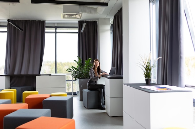 A young woman works at a desk in a large open space in the office