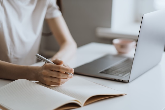 young woman works on a laptop and takes notes in a notebook 