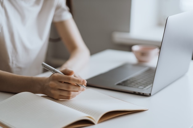 Young woman works on a laptop and takes notes in a notebook 