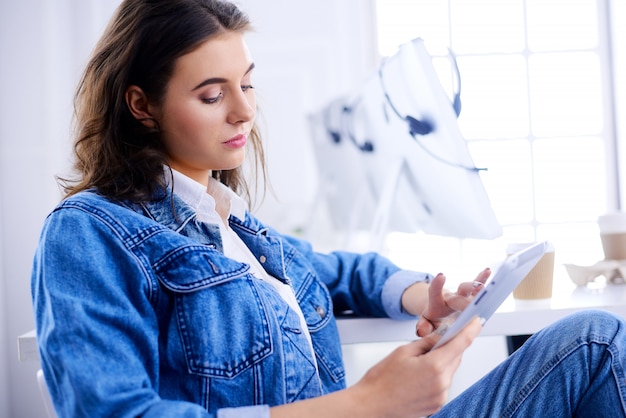 Young woman works in the office with a tablet. Student drinking coffee in the loft