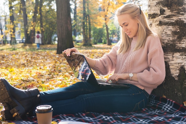 A young woman works in a park typing on a laptop