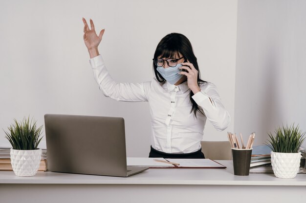 Una giovane donna lavora a distanza in ufficio con una maschera protettiva durante un'epidemia